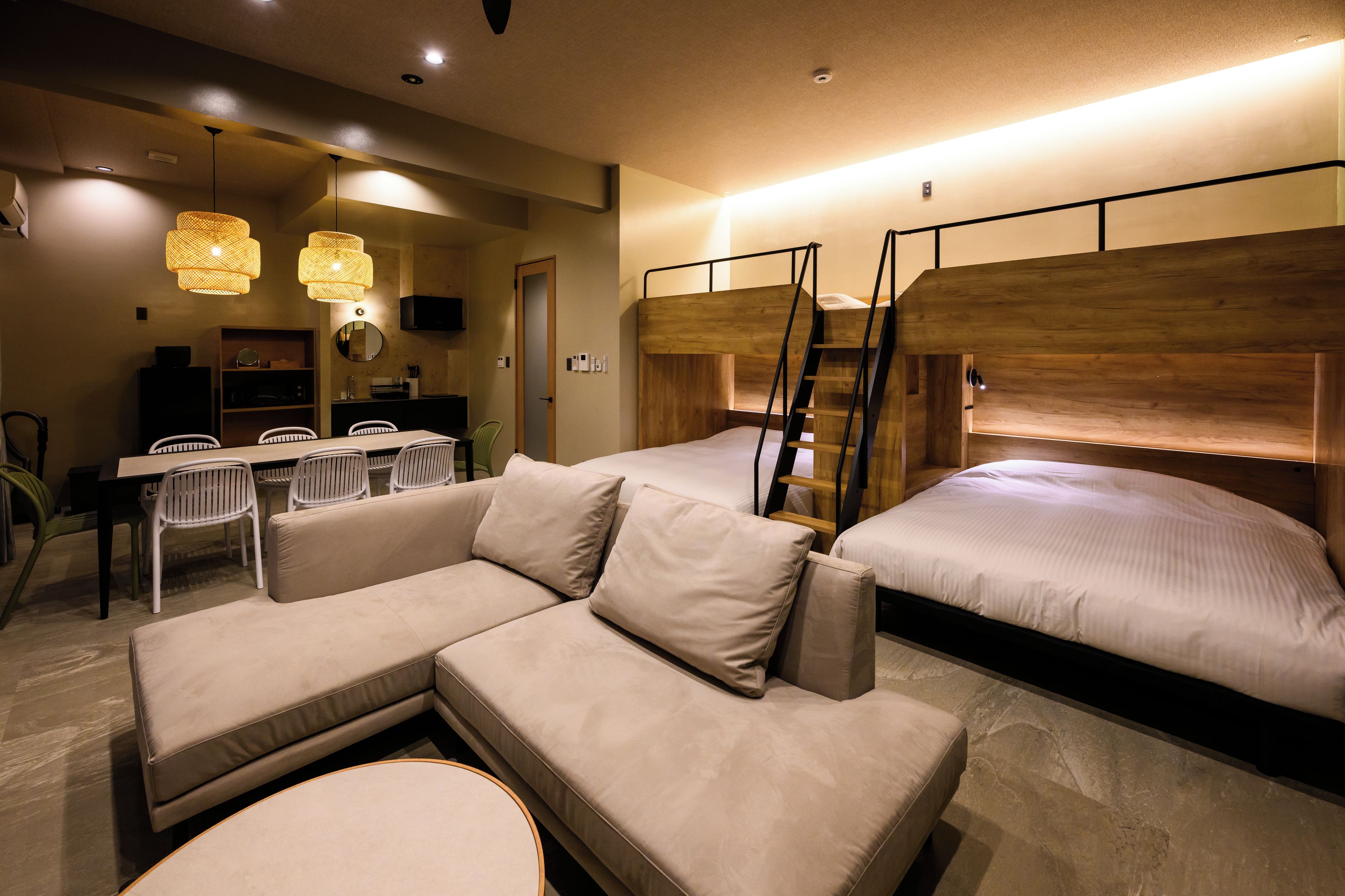Quarto de hotel moderno com sofá, cama com cabeceira de madeira, escrivaninha com cadeiras e mesa de jantar.