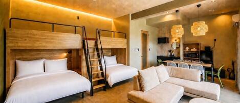 Una habitación de hotel moderna con dos camas, un sofá, una zona de comedor y un ventilador de techo.