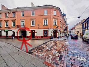 Une rue bordée d’un immeuble à la façade rouge et blanche, doté d’un auvent noir et d’une entrée de magasin.