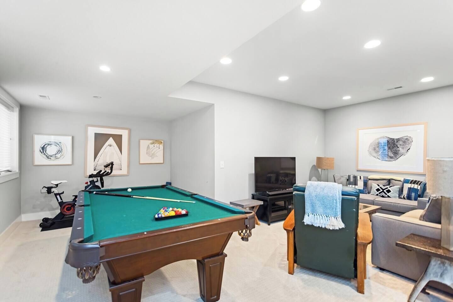 A pool table with a cue stick, a television, and a sofa in a room with white walls and ceiling lights.