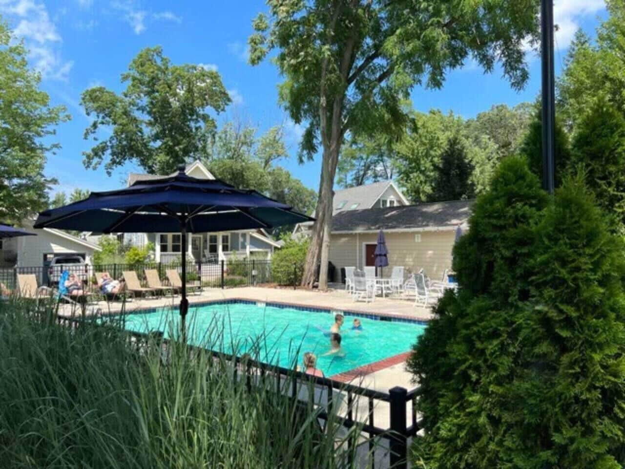 A swimming pool with lounge chairs and umbrellas, surrounded by trees and a fence.