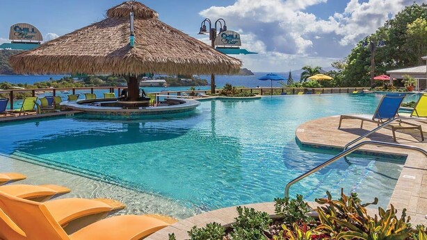 Zona de piscina con sillones de descanso, una sombrilla de paja y vista al océano.