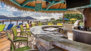 Terraza con mobiliario exterior y zona de bar, con vista a un cuerpo de agua y un paisaje montañoso.