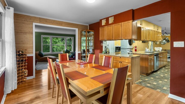 Una cocina amplia con armarios de madera, un comedor con una mesa grande y sillas, y vista al exterior a través de una ventana.