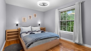Un dormitorio moderno con una cama de madera, paredes grises y un ventanal con cortinas.