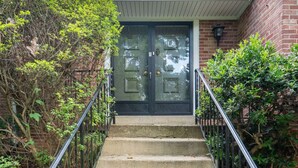 Vista frontal de una casa con puerta doble, un pequeño porche y una escalera que conduce a la entrada.
