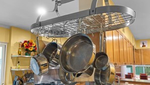 Una cocina con ollas y sartenes colgando, armarios de madera, una estufa y una encimera con diversos objetos.