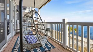 Un balcone con una sedia a dondolo, vista sulla spiaggia e un pontile di legno.