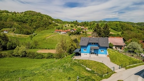 A blue house with a paved driveway, surrounded by green fields and hills. - The Blue House With Sauna & Jacuzzi (Desinic)