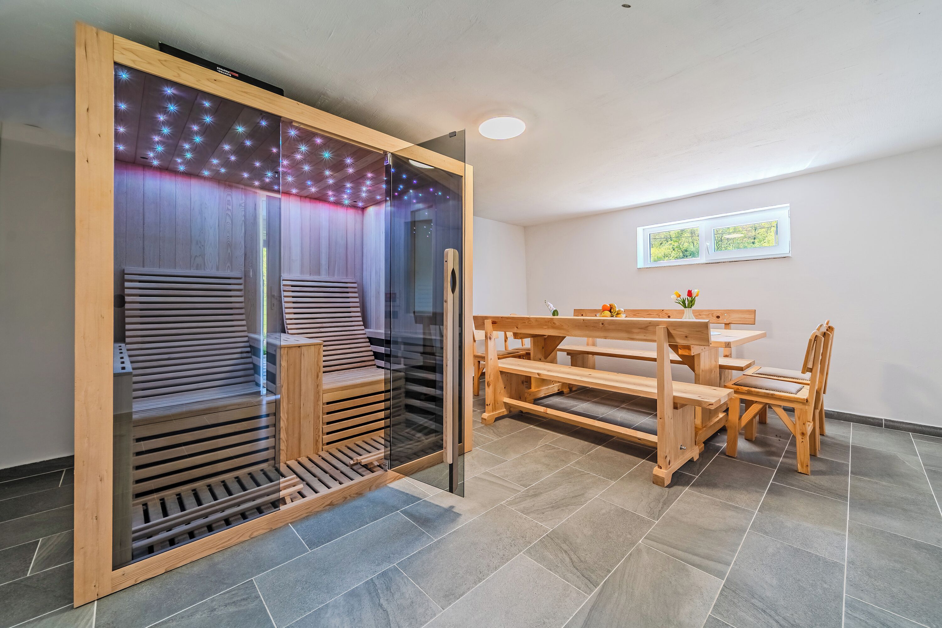 A room with a sliding glass door, a wooden bench, a table, and chairs.