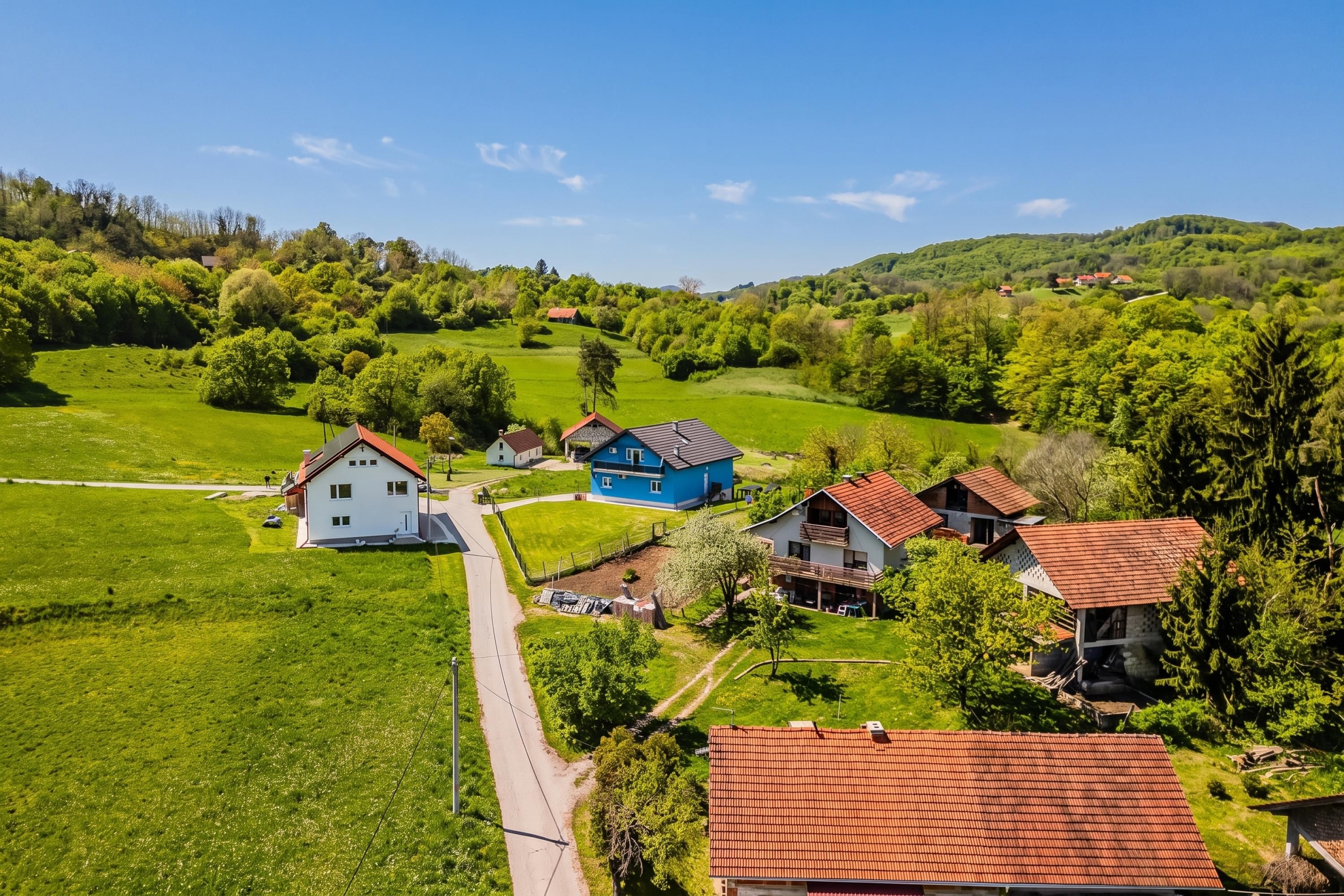 Un paisaje rural con una carretera, campos verdes y varias casas con techos rojos.