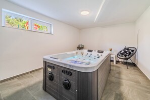 A bathroom with a large bathtub, a window with a view, a chair, and a small table. - The Blue House With Sauna & Jacuzzi (Desinic)