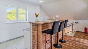 A modern kitchen with a brick accent wall, a wooden counter, and two black bar stools. - The Blue House With Sauna & Jacuzzi (Desinic)