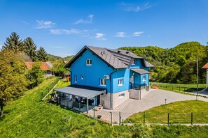 A two-story house with a sloped roof, a covered patio, and a fenced yard. - The Blue House With Sauna & Jacuzzi (Desinic)