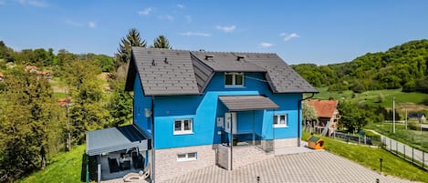 A two-story house with a blue exterior, a sloped roof, and a paved driveway.