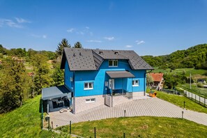 A two-story house with a blue exterior, a sloped roof, and a paved driveway. - The Blue House With Sauna & Jacuzzi (Desinic)