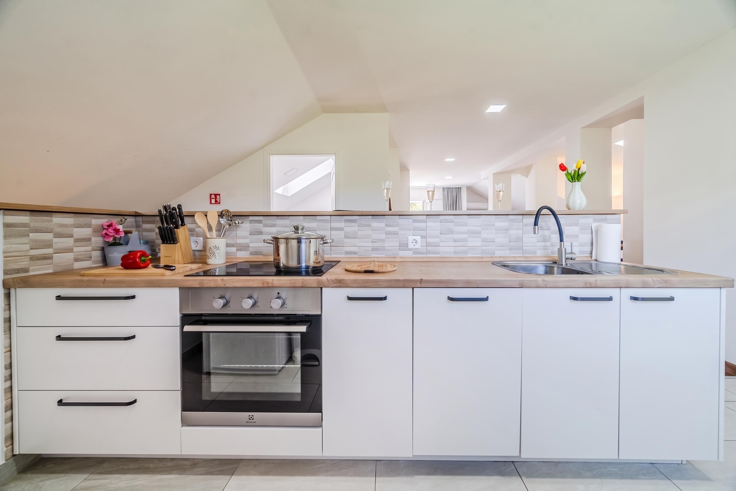 Una cocina moderna con horno empotrado, pileta y encimera con diversos utensilios.