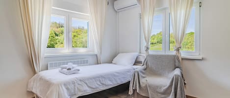 A bedroom with a single bed, a chair, and an air conditioning unit.