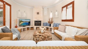 A living room with a fireplace, a television, wicker furniture, and a stone accent wall. - Villa Sanchez – Comfort and tranquility by the sea. (Santanyi)