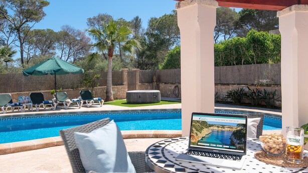 A poolside area with lounge chairs, a laptop, and a glass of beer on a table. - Villa Sanchez – Comfort and tranquility by the sea. (Santanyi)