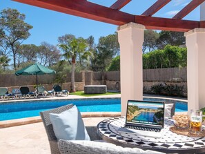 Ein Poolbereich mit Liegestühlen, einem Laptop und einem Glas Bier auf einem Tisch.