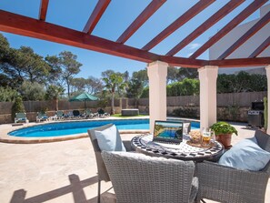 Ein überdachter Außenbereich mit Pool, Liegestühlen und einem Tisch mit Laptop und Getränken.