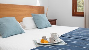 Ein ordentlich bezogenes Bett mit einem hölzernen Kopfteil, zwei Kissen, einem Nachttisch mit einer Vase und einer Ablage mit Orangenscheiben und Tassen.