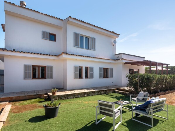 A two-story white house with shutters, a patio with chairs, and a small garden. - Ca Na Lida – Beautiful villa for 8 guests in Cala Santanyí (Santanyi)