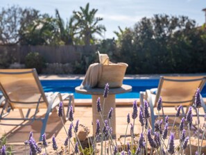 A poolside area with two lounge chairs, a stone table with a cushion, and lavender plants in the foreground. - Ca Na Lida – Beautiful villa for 8 guests in Cala Santanyí (Santanyi)