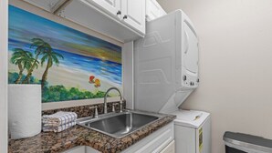 Eine Küche mit einer Granit-Arbeitsplatte, einem Edelstahl-Spülbecken, einem Strandbild und einem weißen Kühlschrank.