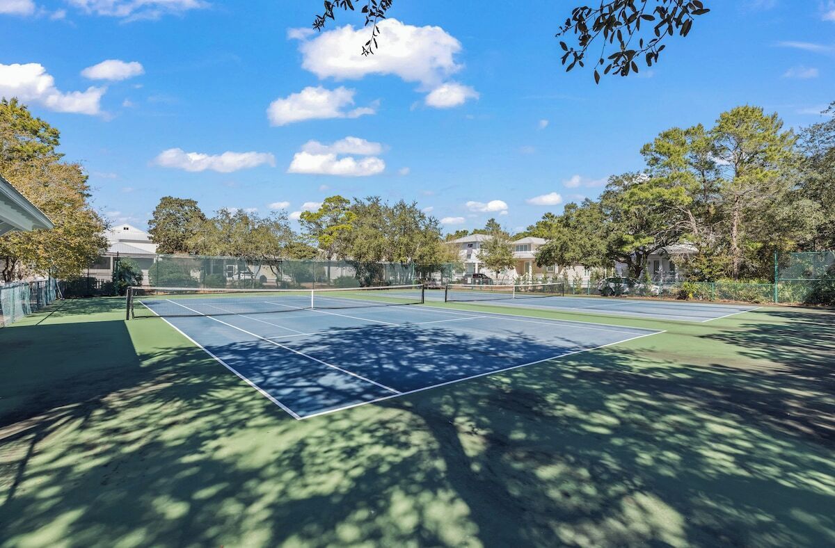 Una cancha de tenis con red, rodeada de árboles y casas.