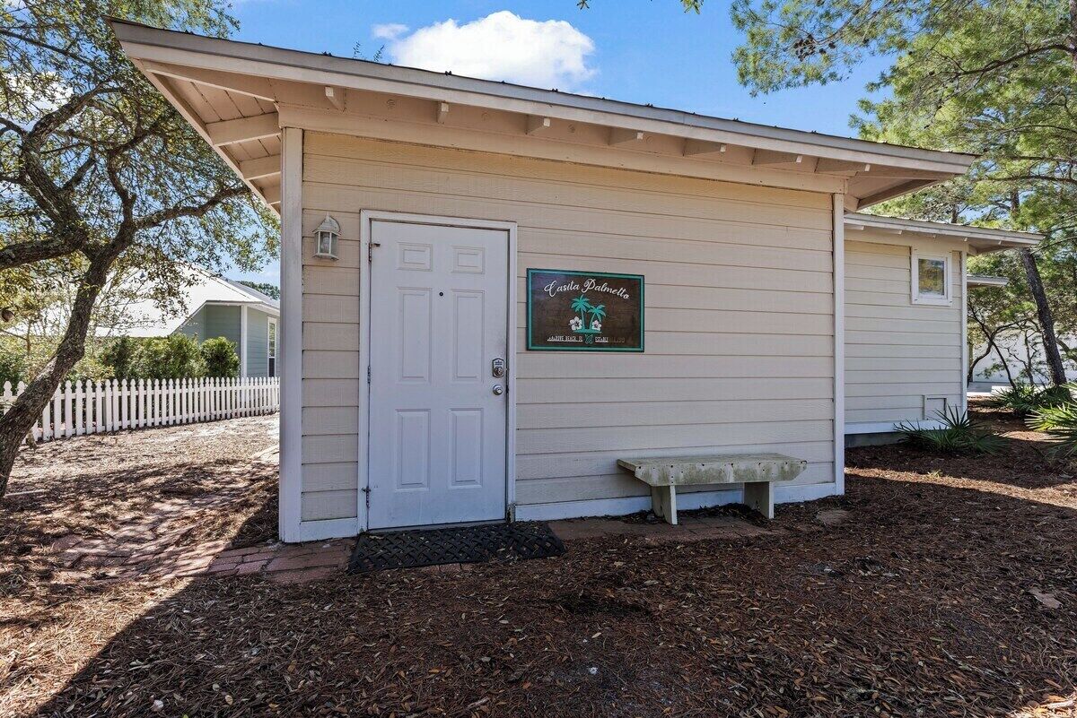 A small building with a white door, a bench, and a sign on the wall.