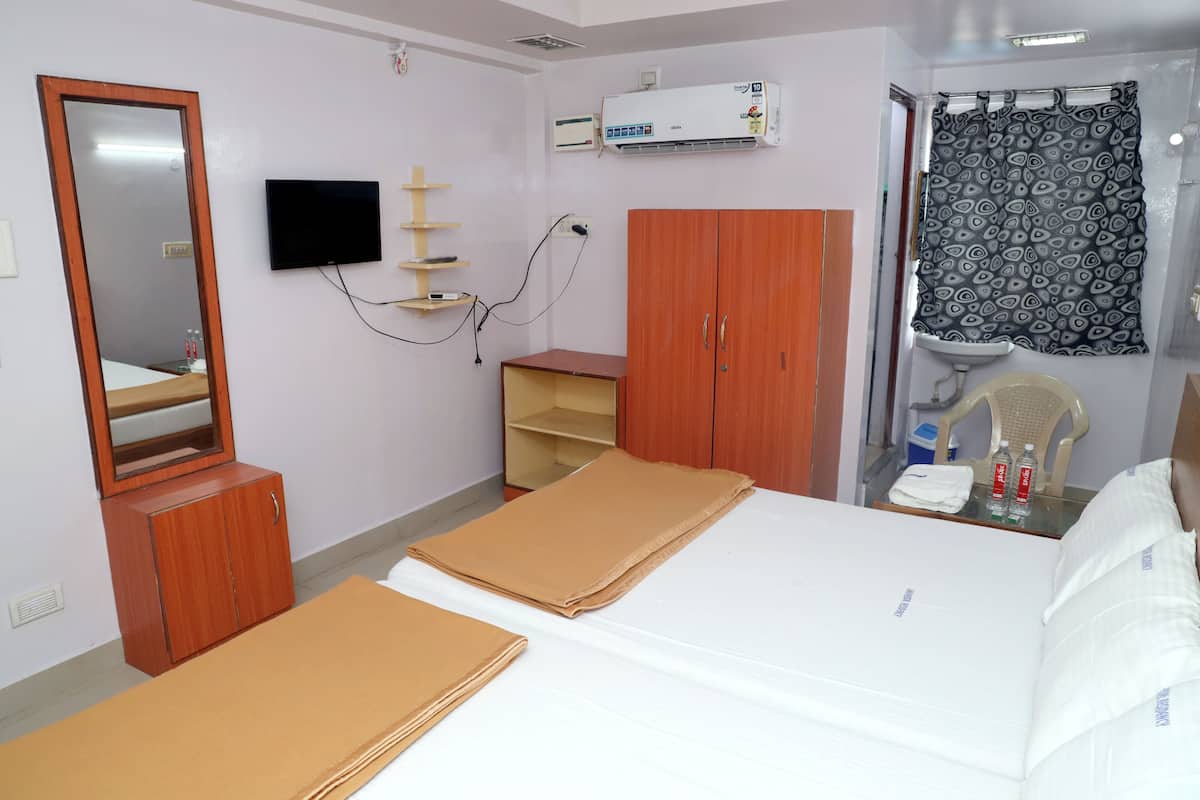 Une chambre d’hôtel comprenant un lit, une armoire en bois, un téléviseur, un appareil de climatisation, une salle de bain avec un rideau de douche et un miroir.
