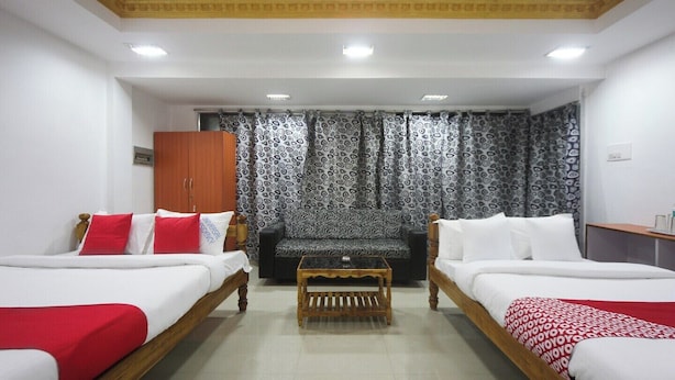 Une chambre d’hôtel avec deux lits simples, une table basse en bois, un canapé, des rideaux à motifs et une armoire en bois.