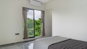 A bedroom with a bed, a large window with curtains, and a view of greenery outside. - Parvata Vista By Soumil's Stays (Karjat)