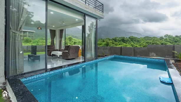 A modern pool area with a glass-enclosed room, outdoor seating, and a view of lush greenery. - Parvata Vista By Soumil's Stays (Karjat)