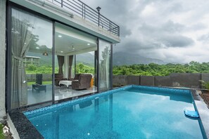 Un área de piscina moderna con una sala acristalada, mobiliario exterior y vistas a vegetación exuberante.