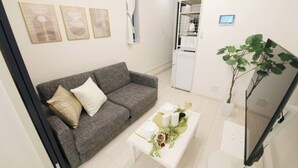 Un soggiorno moderno con un divano grigio, un tavolino da caffè bianco con oggetti decorativi, una TV a schermo piatto e una piccola pianta.
