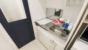 Una piccola cucina compatta con lavandino, specchio e un piano di lavoro con una scatola di fazzoletti, una bottiglia di sapone per le mani e un piccolo contenitore.