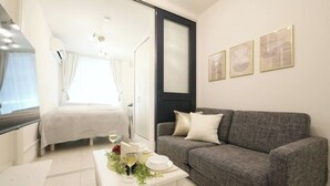 Una camera moderna e luminosa con un divano grigio, un tavolino bianco con un bicchiere di vino e un letto con biancheria bianca.