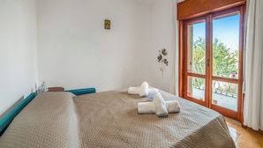 Une chambre d’hôtel avec un grand lit, une fenêtre donnant sur des arbres et une petite table avec une bouteille.