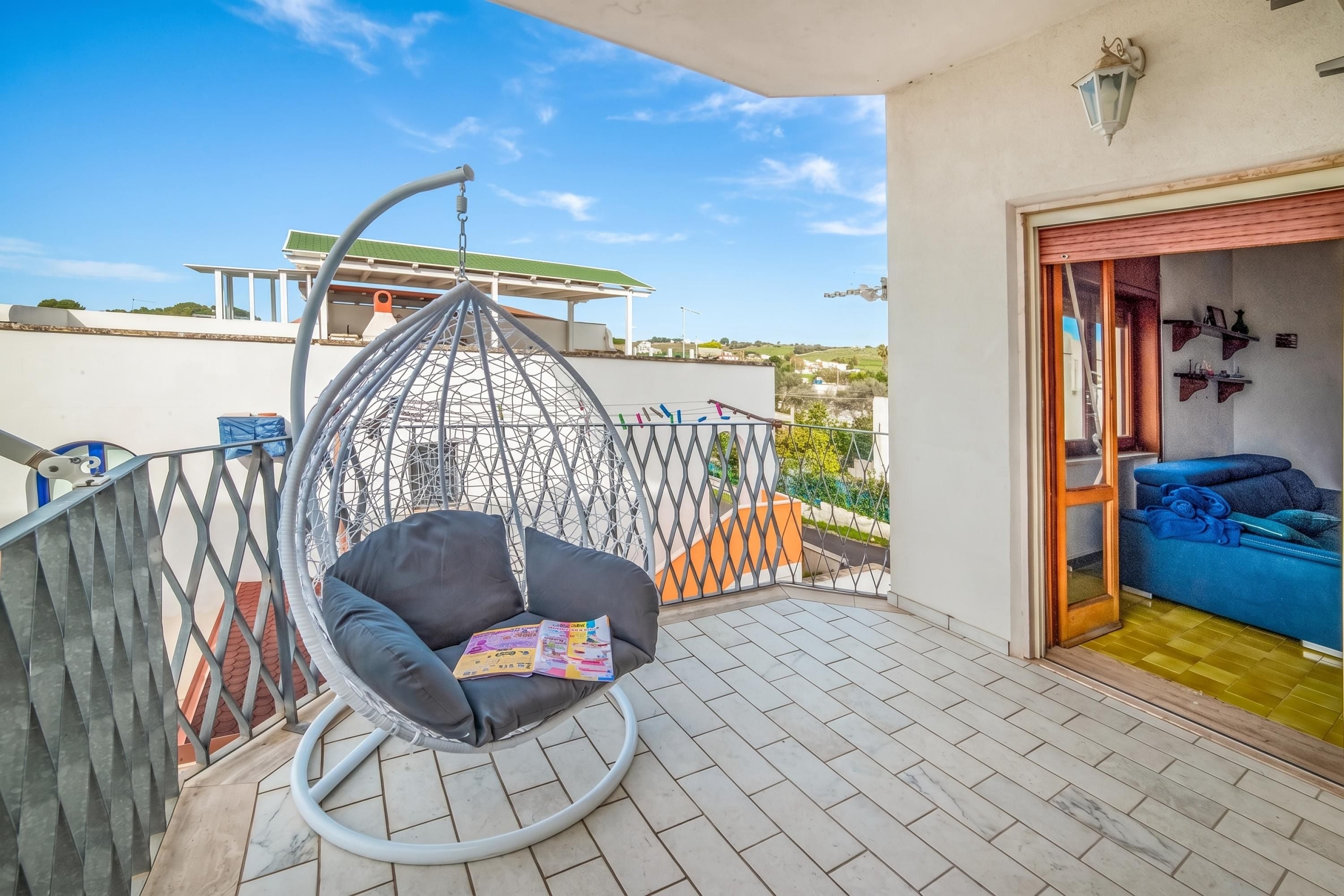 Ein Balkon mit einer Hängematte, einem blauen Sofa und Blick auf ein Gebäude mit einem begrünten Dach.