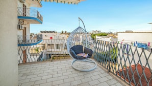 Un balcon avec un fauteuil suspendu, une clôture en métal et une vue sur des bâtiments au loin.