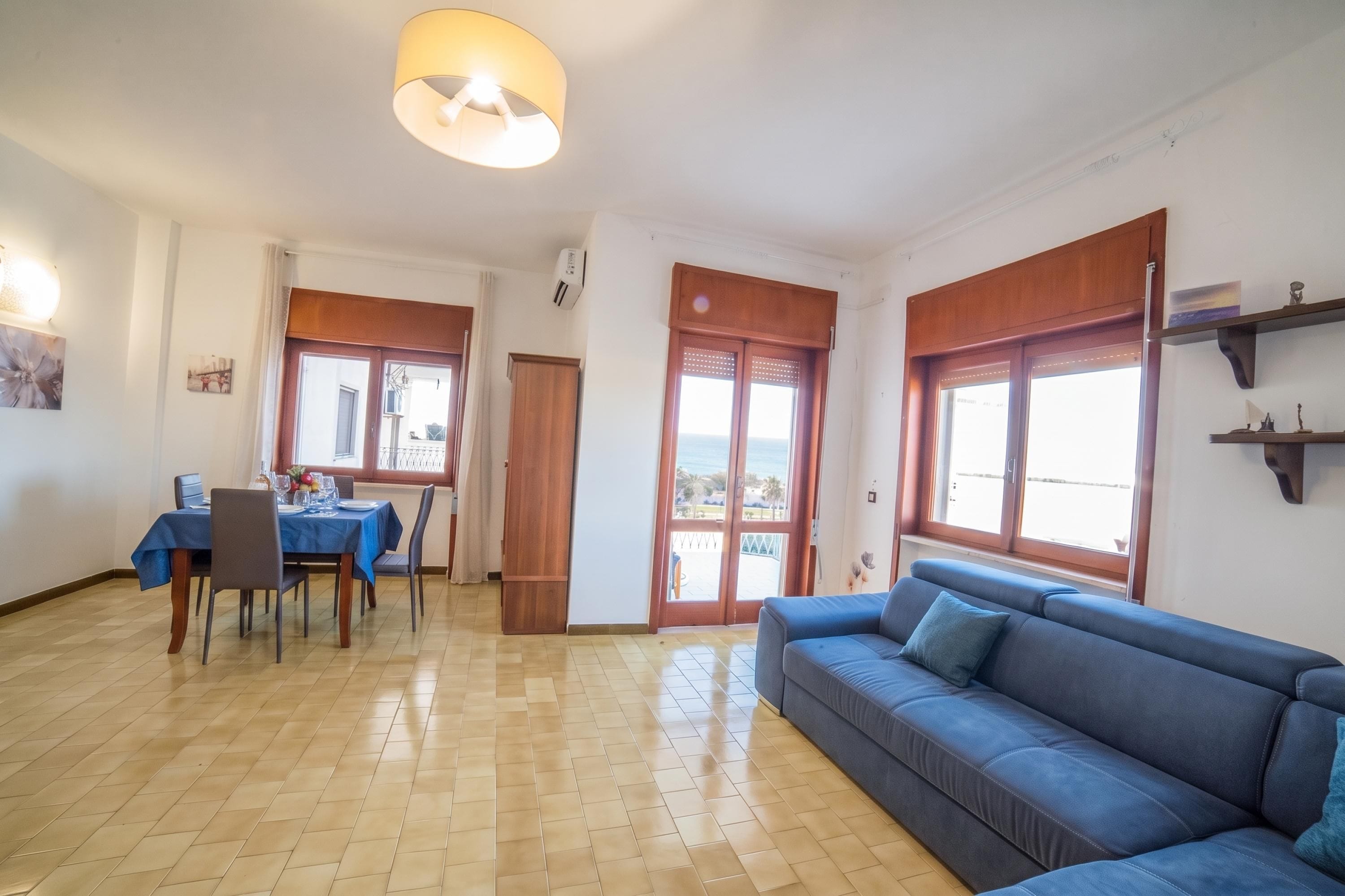 A living room with a blue sofa, dining table with chairs, and a large window with a view.