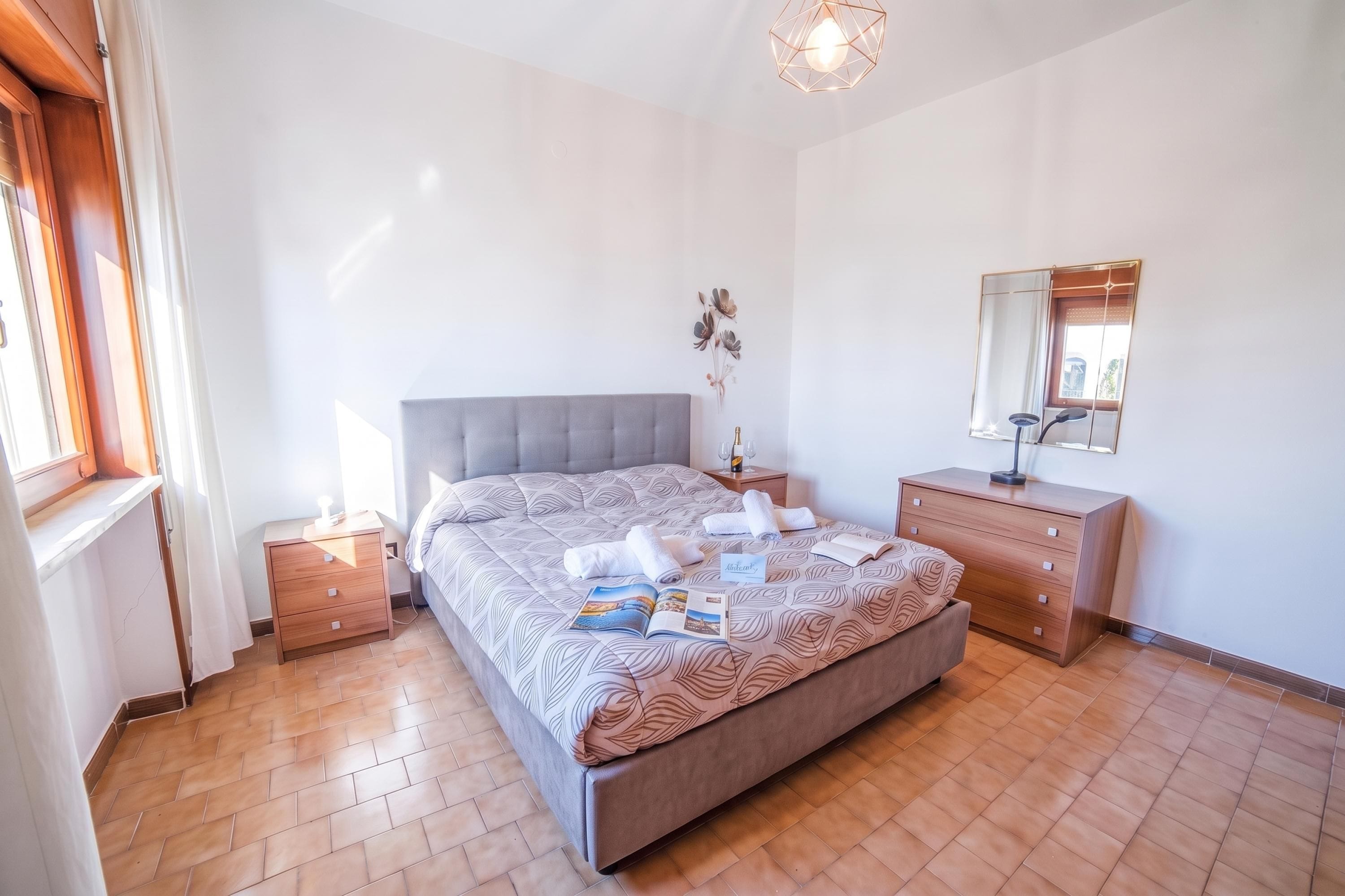Quarto com cama, mesa de cabeceira, penteadeira, espelho e janela.