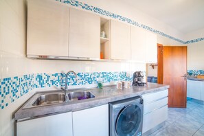 A compact kitchen with a built-in washing machine, a sink, and a coffee maker. - Tramonto D'oro Apartment Near The Beach (Porto Cesareo)