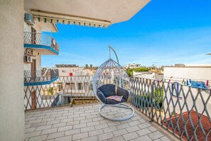 A balcony with a hanging chair, a view of the city, and a tiled floor. - Tramonto D'oro Apartment Near The Beach (Porto Cesareo)