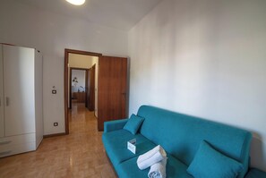 A room with a teal sofa, a white wardrobe, and a wooden door leading to another room. - Tramonto D'oro Apartment Near The Beach (Porto Cesareo)