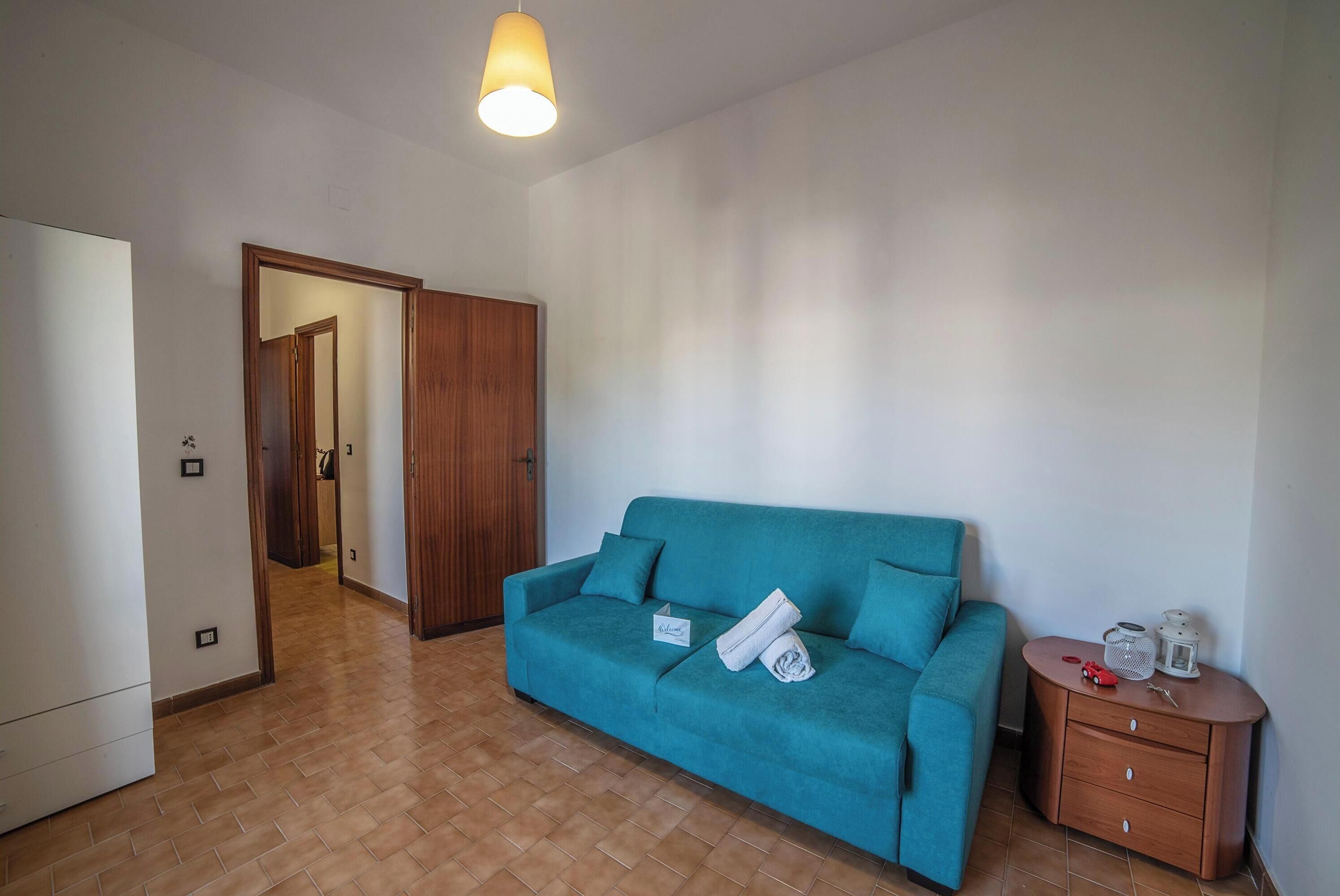 A room with a teal sofa, a wooden cabinet, and a tiled floor.