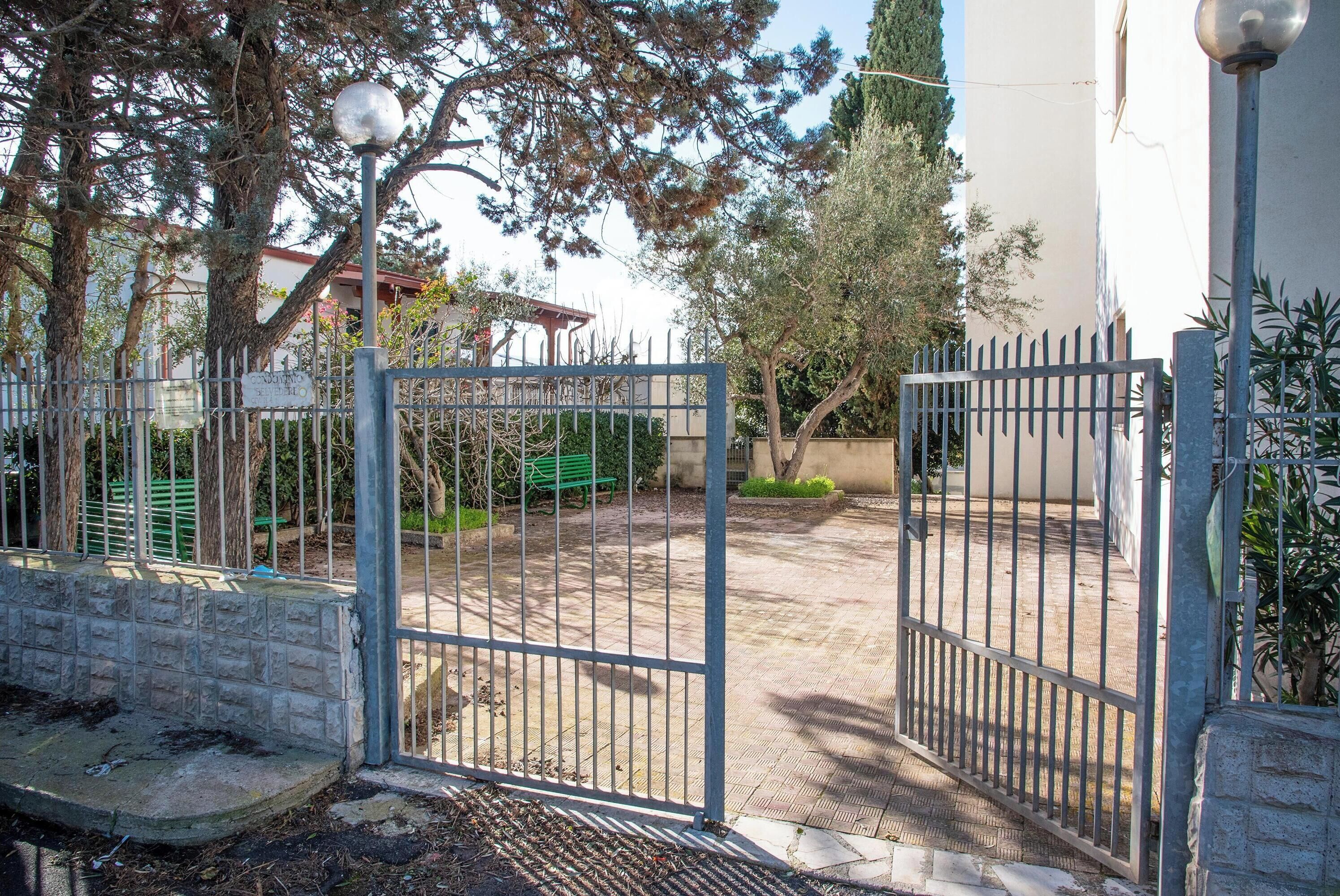 A gated entrance with a metal gate, a paved pathway, and a bench.